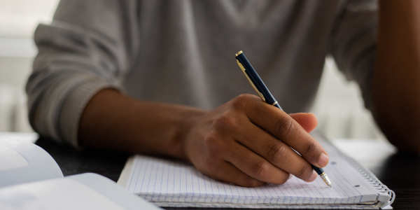 Main d'adulte écrivant au stylo sur un cahier